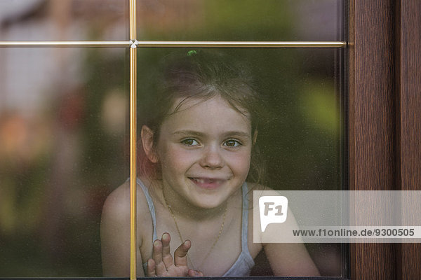 Glückliches kleines Mädchen  das aus dem Fenster schaut.