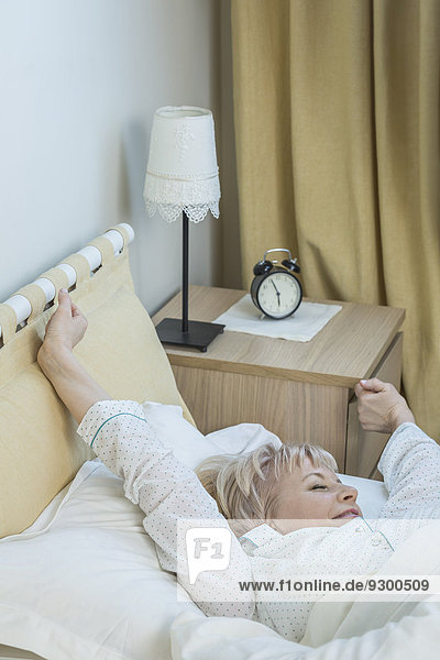 Senior woman stretching while lying in bed at home