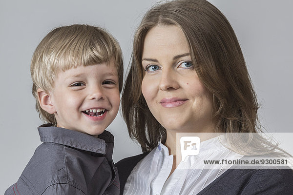 Portrait of son and mother smiling against gray background