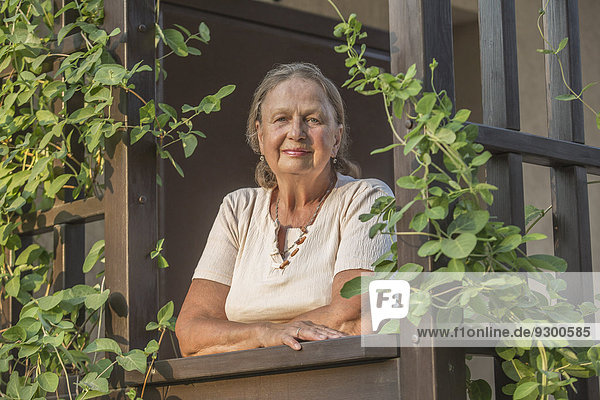 Porträt einer älteren Frau  die zu Hause auf dem Balkon steht.