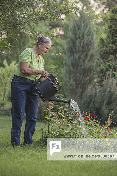 Seniorin beim Blumen gießen im Garten