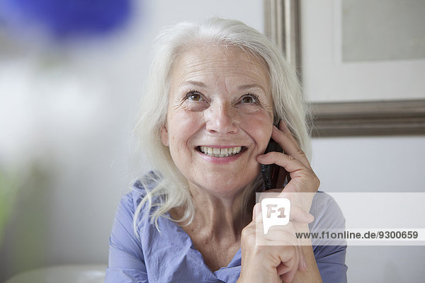 Glückliche Seniorin schaut auf,  während sie zu Hause ans Handy geht.