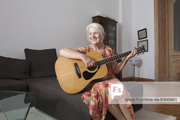Senior women playing guitar in living room at home
