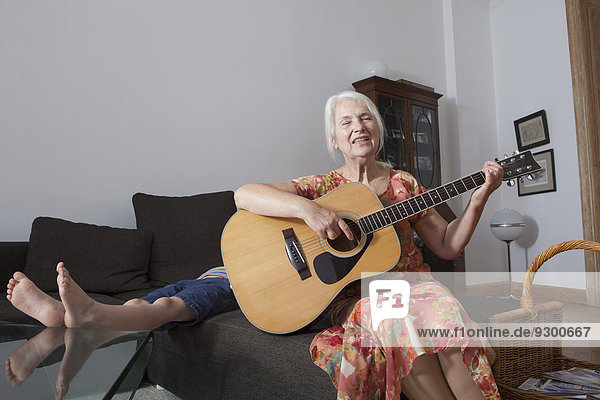 Seniorin singt Lied  während sie zu Hause Gitarre spielt.