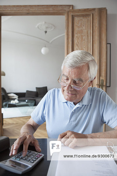 Älterer Mann  der die Hausfinanzen am Tisch berechnet.