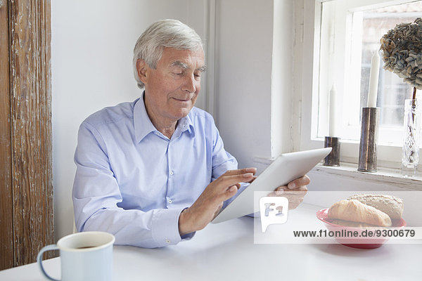 Älterer Mann mit digitalem Tablett am Frühstückstisch