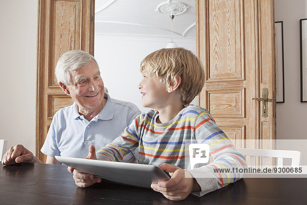 Glücklicher älterer Mann sieht Enkel mit digitalem Tablett zu Hause an