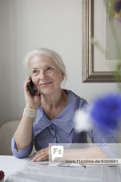 Lächelnde Seniorenfrau beim Telefonieren am Tisch