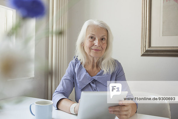 Porträt der selbstbewussten Seniorin mit digitalem Tablett am Tablett