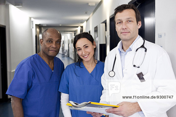 Two doctors in scrubs and a doctor in a lab coat in a hospital hallway