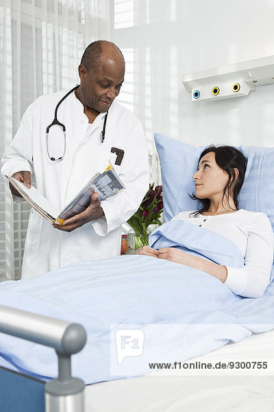 Ein Arzt im Gespräch mit einem Patienten  der in einem Krankenhausbett liegt.