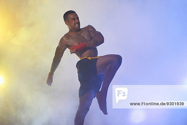 Studioaufnahme eines muskulösen männlichen Kickboxers im Scheinwerferlicht und Nebel
