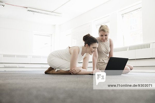Zwei junge Geschäftsfrauen mit Laptop auf dem Boden im neuen Büro