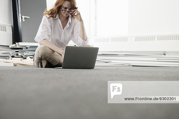 Mittlere erwachsene Geschäftsfrau mit Laptop auf dem Boden in neuem Büro