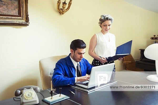 Young vintage couple at desk with files and laptop