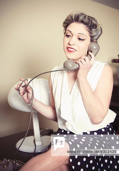 Portrait einer jungen Frau,  die Vintage-Kleidung trägt und am Vintage-Telefon spricht.
