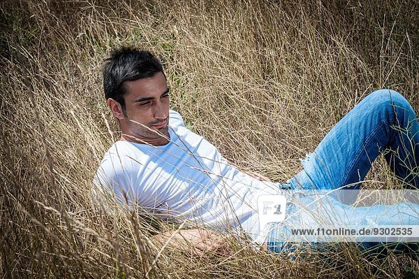Porträt eines jungen Mannes im langen Gras liegend