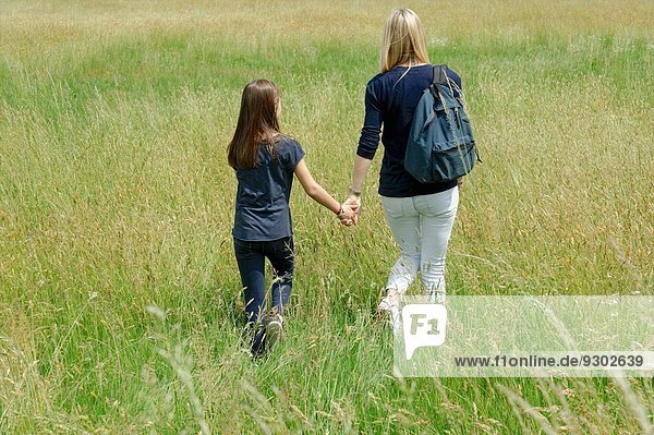 Rückansicht von Mutter und Tochter beim Spaziergang durch das lange Grasfeld