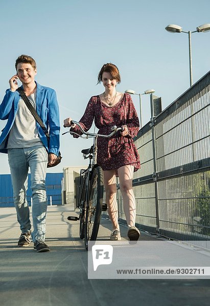 Young couple pushing bicycle over bridge