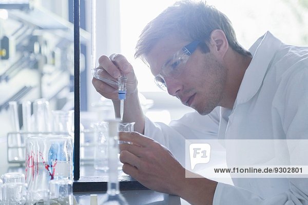 Junger Wissenschaftler pipettiert in Becherglas im Labor