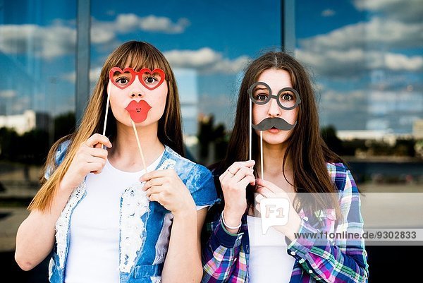 Porträt von zwei jungen Frauen  die Lippen- und Augenmasken hochhalten.