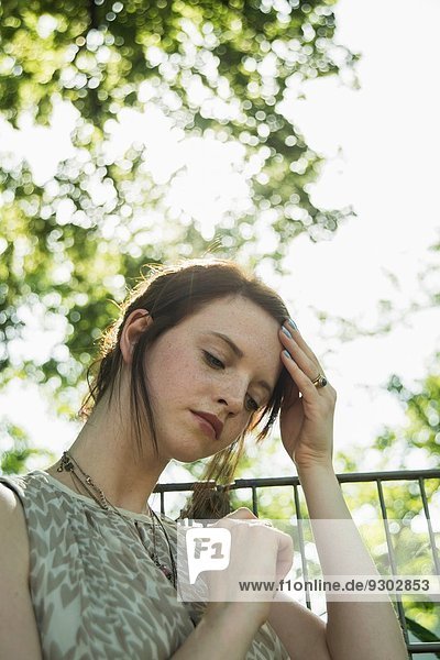 Porträt einer mürrischen jungen Frau mit Hand auf dem Kopf im Park