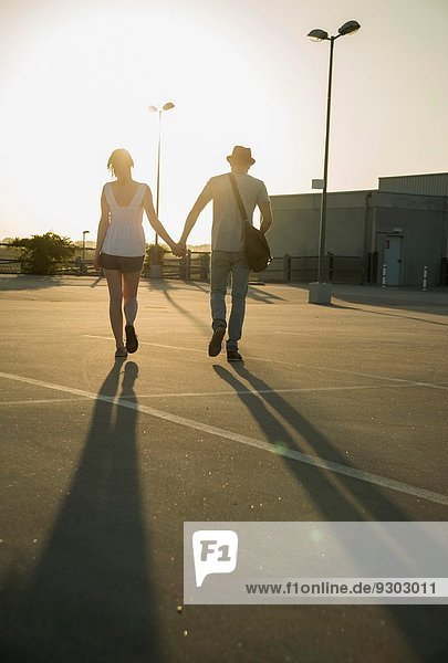 Romantisches junges Paar schlendert Hand in Hand über den leeren Parkplatz