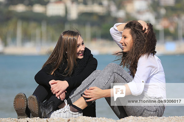 Zwei Freundinnen  Teenager  sitzen am Strand  Menton  Alpes-Maritimes  Provence-Alpes-Côte d'Azur  Frankreich
