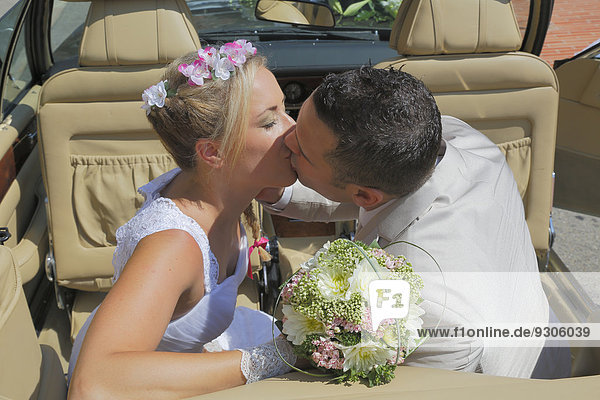 Braut und Bräutigam küssen sich auf der Rückbank eines offenen Autos