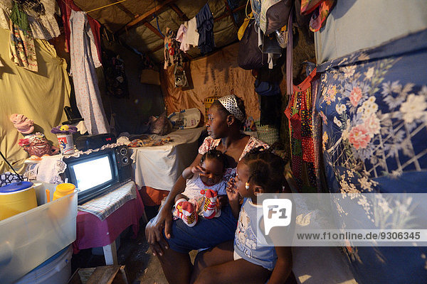 Frau mit zwei Kindern vor dem Fernseher in einer ärmlichen Baracke  Lager für Erdbebenflüchtlinge Camp Icare  Fort National  Port-au-Prince  Haiti