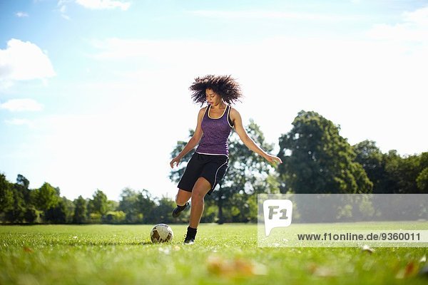 Young woman kicking soccer ball in park
