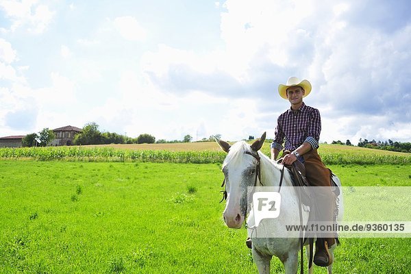 Porträt eines jungen Mannes in Cowboy-Ausrüstung zu Pferd im Gelände