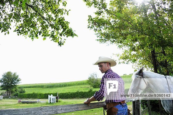 Junger Mann in Cowboy-Ausrüstung mit Pferdekontrollzaun