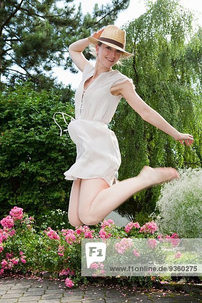 Mittlere erwachsene Frau  die mitten in der Luft im Garten springt.
