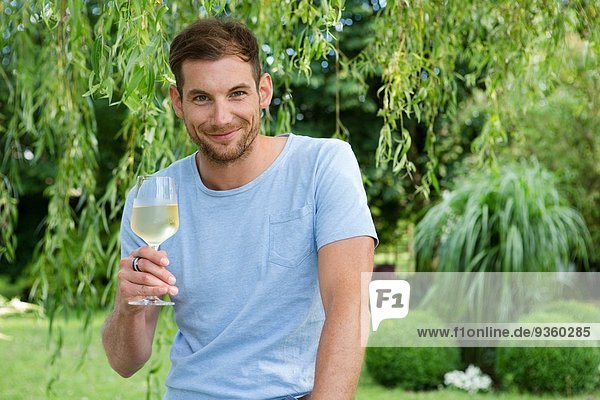 Porträt eines erwachsenen Mannes mit einem Glas Weißwein im Garten