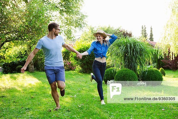 Mid adult couple holding hands whilst running in garden