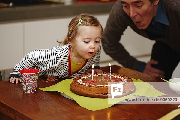 Junges Mädchen beim Ausblasen von Geburtstagskerzen auf Kuchen