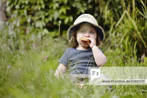 Junges Mädchen sitzt im Gras und isst einen Snack.