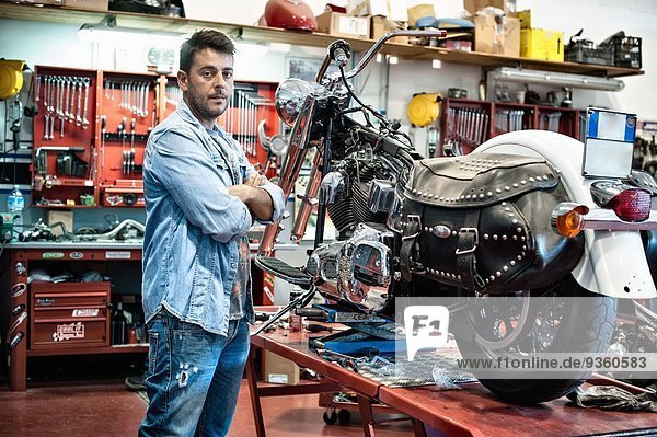 Portrait eines Mechanikers mit gekreuzten Armen in der Motorradwerkstatt