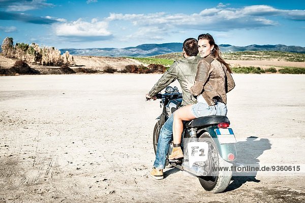 Rear view of young couple riding motorcycle on arid plain  Cagliari  Sardinia  Italy