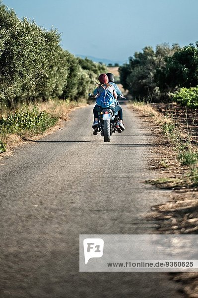 Rear view of mid adult couple riding motorcycle on rural road  Cagliari  Sardinia  Italy