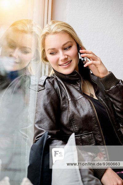 Junge Frau auf einem Smartphone  während sie aus dem Fenster schaut.