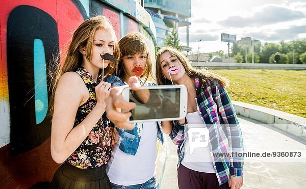 Freunde nehmen Selfie mit gefälschten Lippen und Schnurrbart  Wandgemälde im Hintergrund