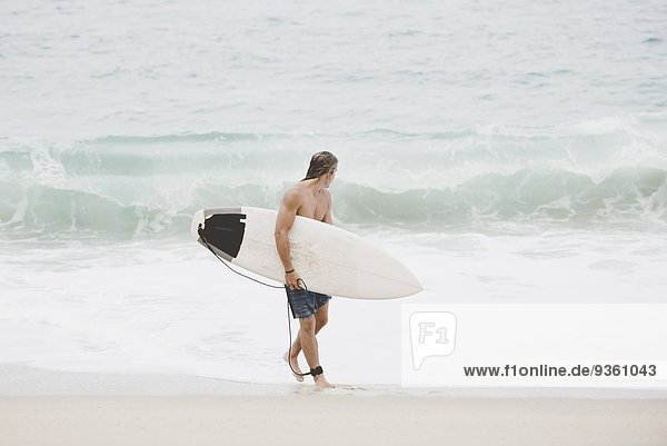 Australischer Surfer mit Surfbrett am Strand