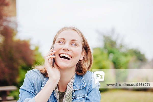 Young woman laughing whilst chatting on smartphone in park