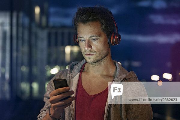 Portrait of young man with smartphone and earphones listening music at night