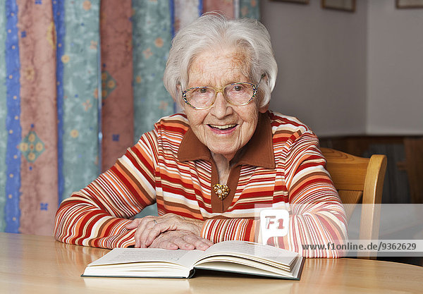 Porträt einer lächelnden Seniorin mit aufgeschlagenem Buch