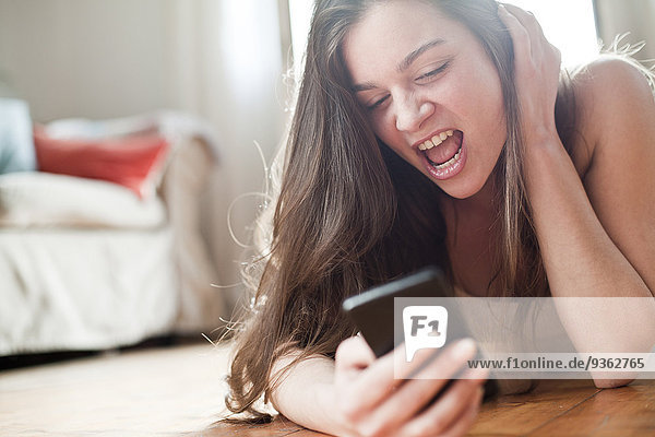 Porträt einer schreienden jungen Frau mit ihrem Smartphone zu Hause