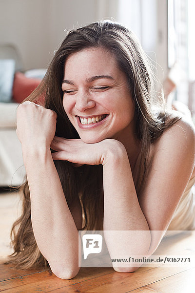 Porträt einer lachenden jungen Frau  die auf dem Boden ihres Wohnzimmers liegt.