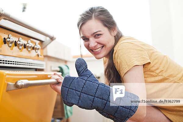 Portrait of smiling young woman in front of her oven
